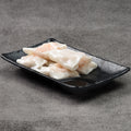 Rice noodle rolls on a black rectangular plate against a gray background