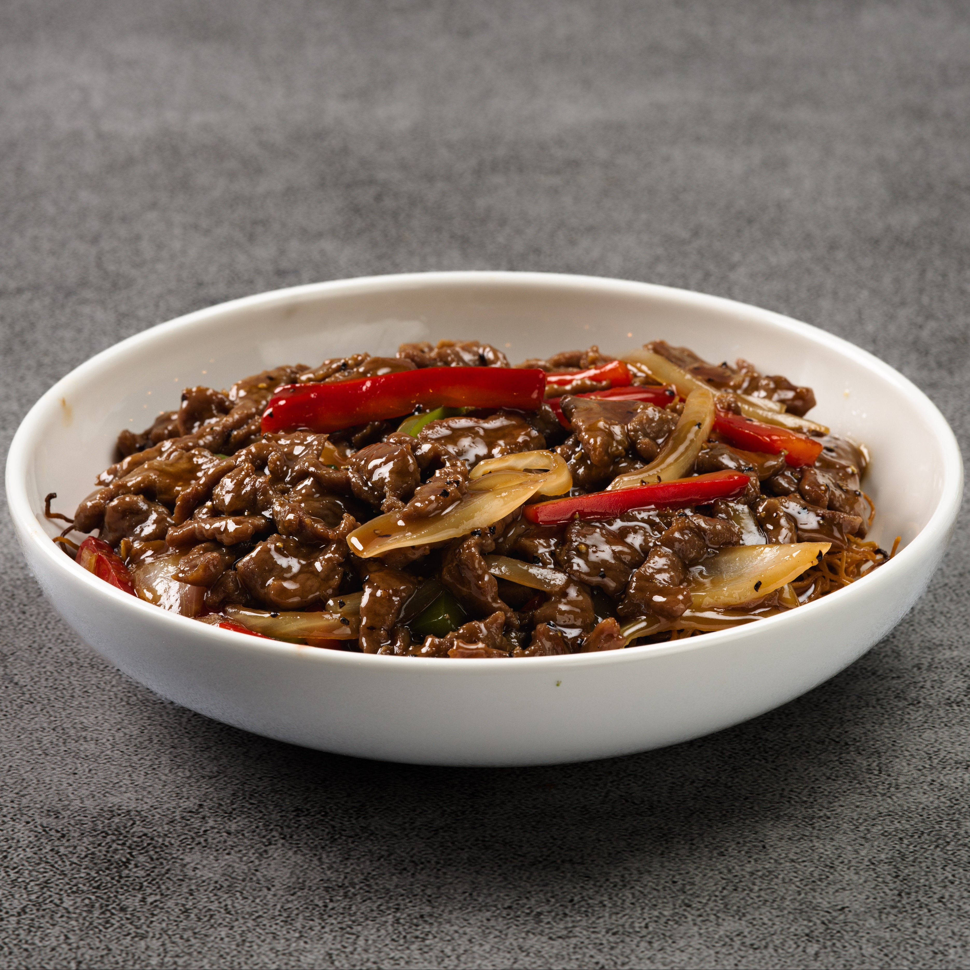 White bowl filled with a dish of beef and vegetables on a gray background