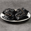 Four black dumplings on a white plate against a gray background