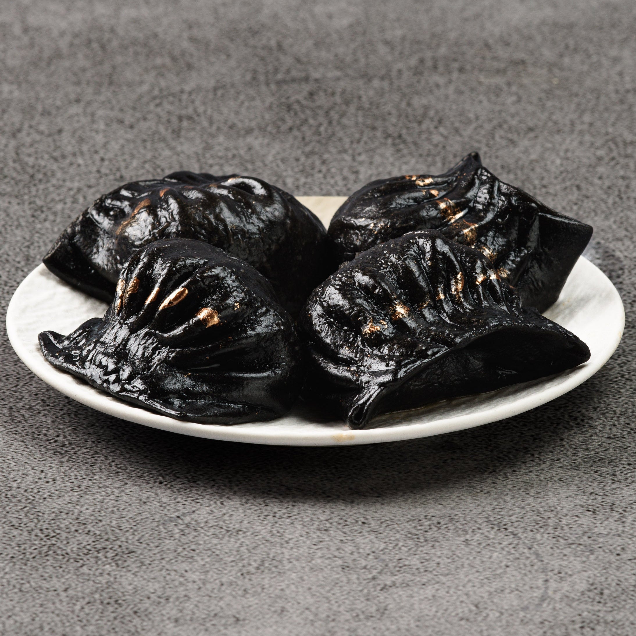 Four black dumplings on a white plate against a gray background