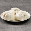 Three steamed buns on a white plate against a gray background