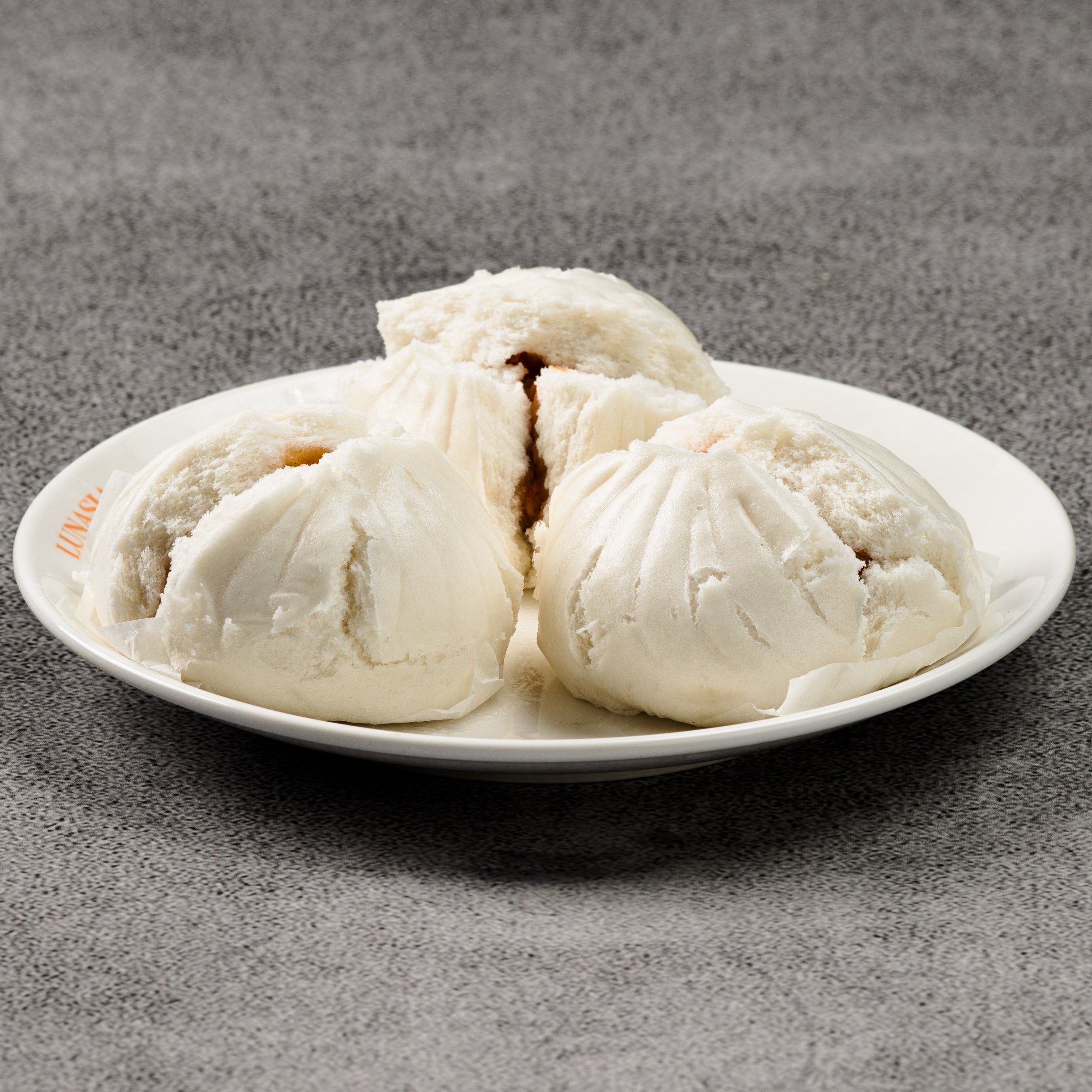 Three steamed buns on a white plate against a gray background