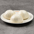 Three white dumplings on a white plate on a gray surface