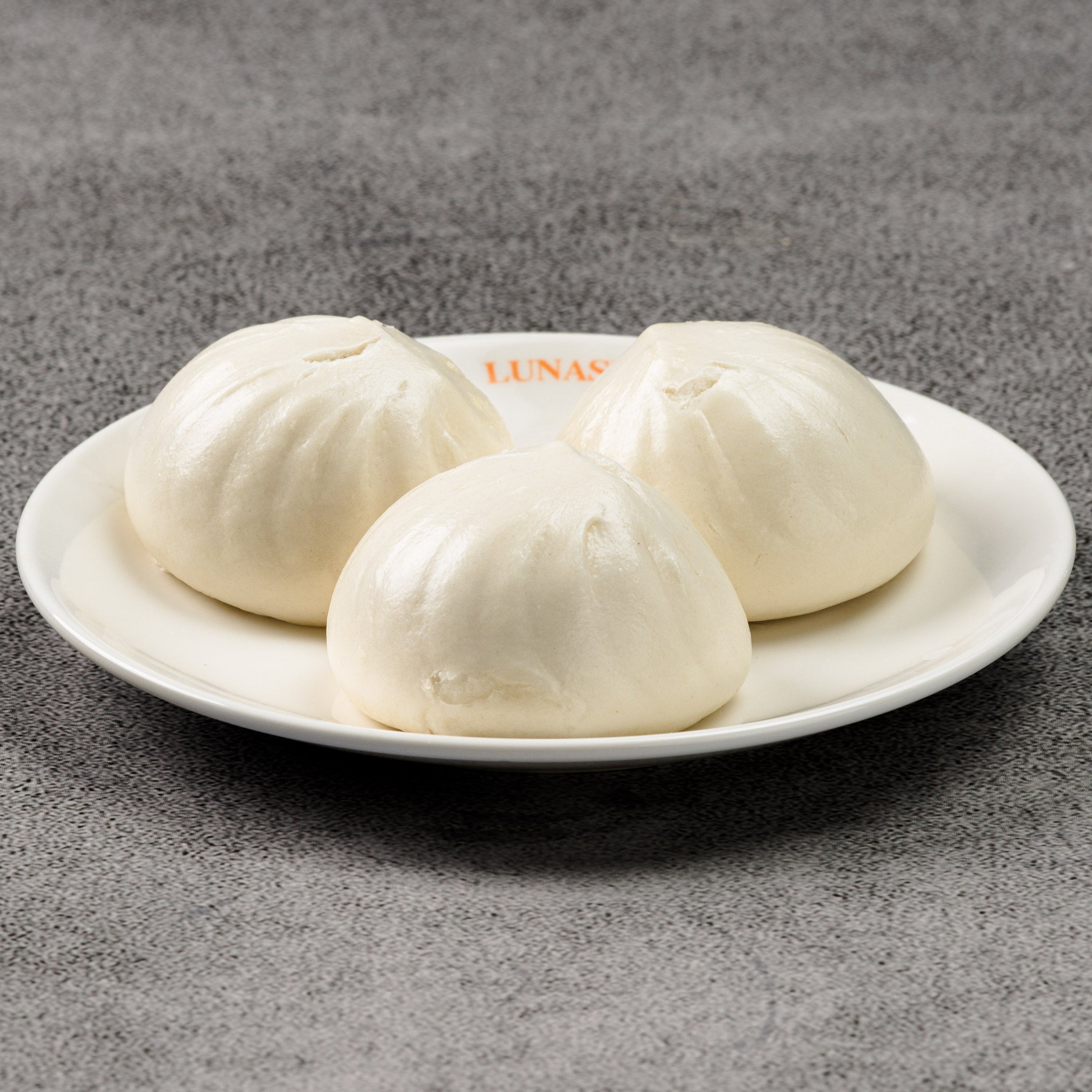 Three white dumplings on a white plate on a gray surface