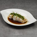 Steamed fish with green herbs on a white plate with a dark background