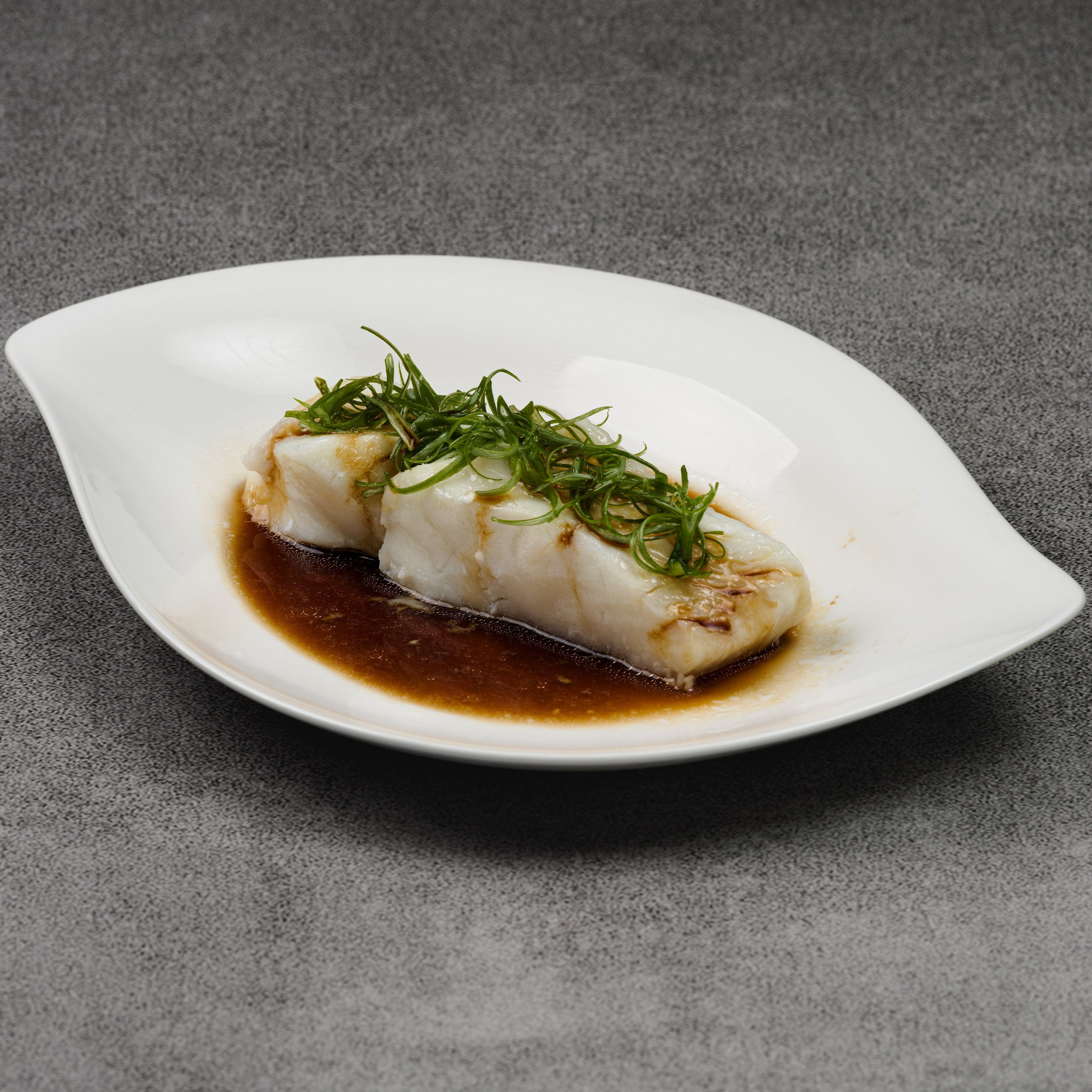 Steamed fish with green herbs on a white plate with a dark background