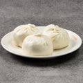 Three white dumplings on a white plate against a gray background