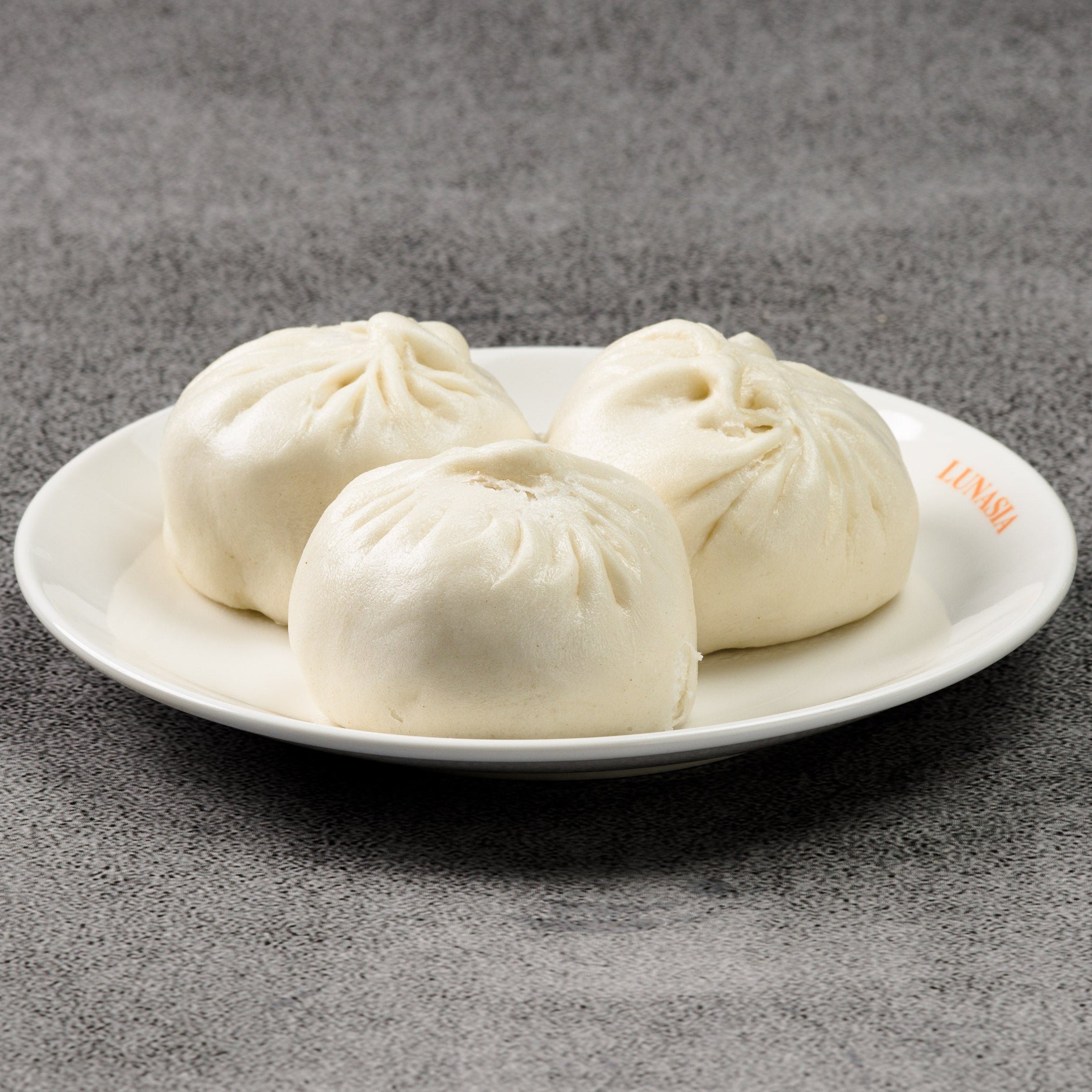 Three white dumplings on a white plate against a gray background