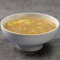 White bowl of sweet corn chicken soup on a gray surface
