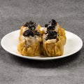 Four steamed buns with black toppings on a white plate against a gray background