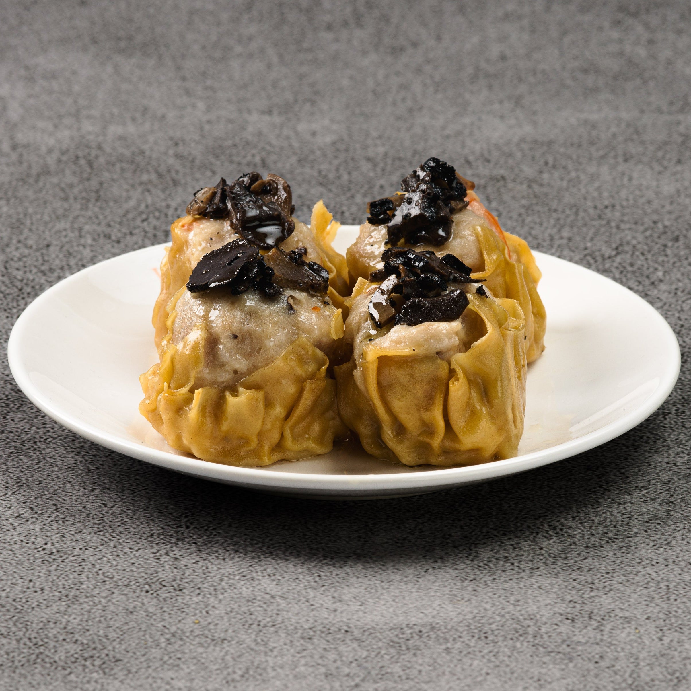 Four steamed buns with black toppings on a white plate against a gray background