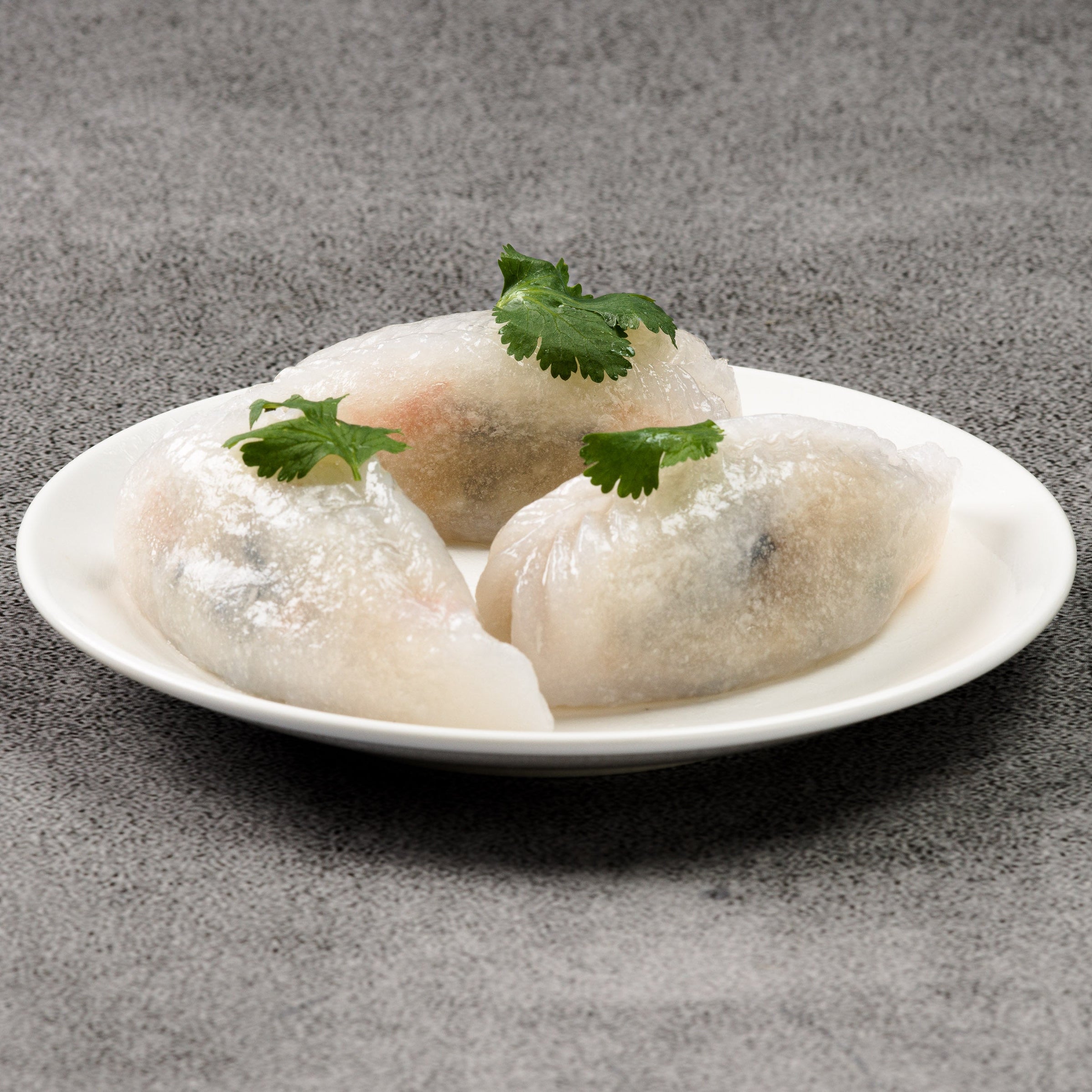 Three dumplings on a white plate on a gray surface