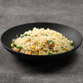 Black bowl of fried rice with vegetables on a gray background