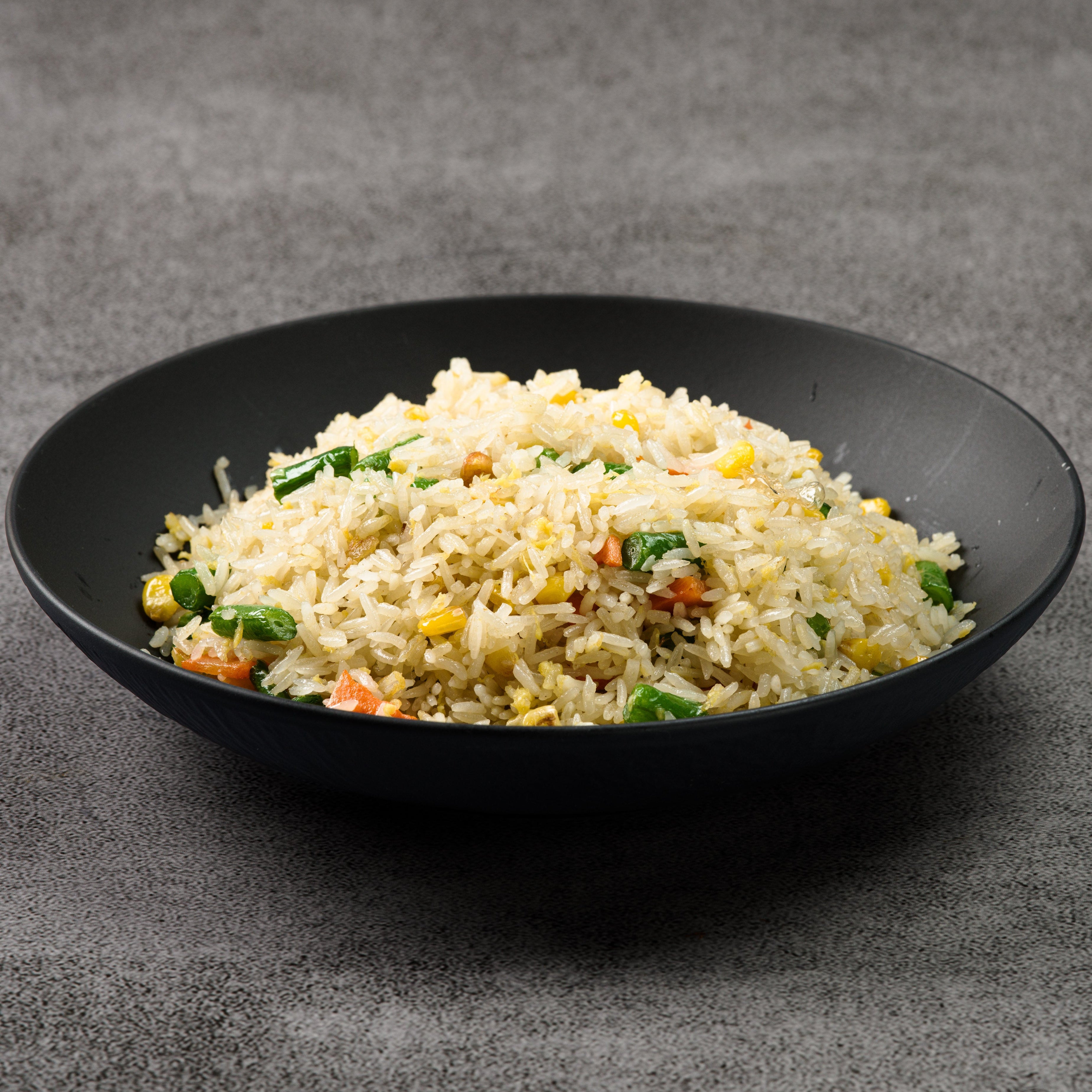 Black bowl of fried rice with vegetables on a gray background