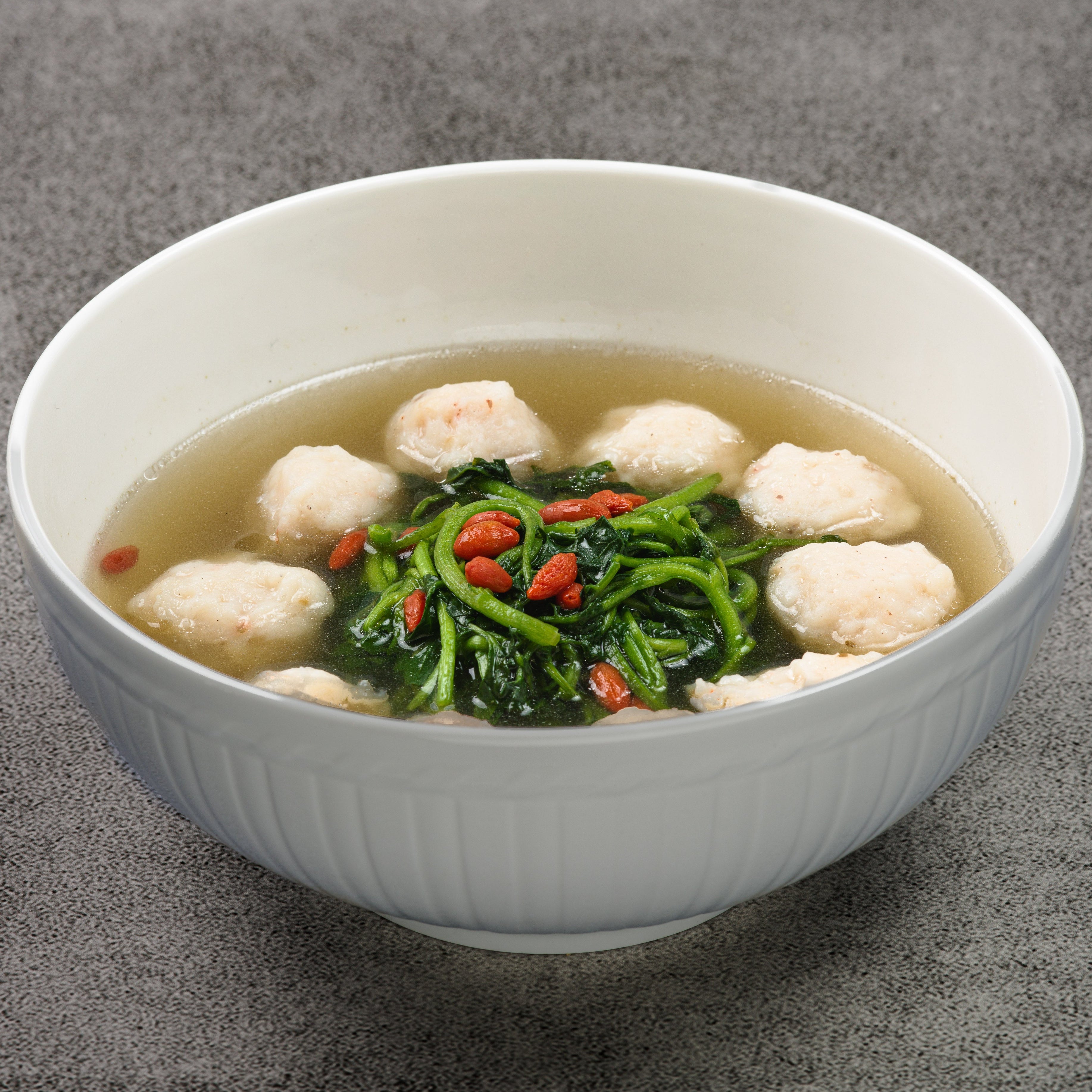 Bowl of soup with tofu and greens on a gray background