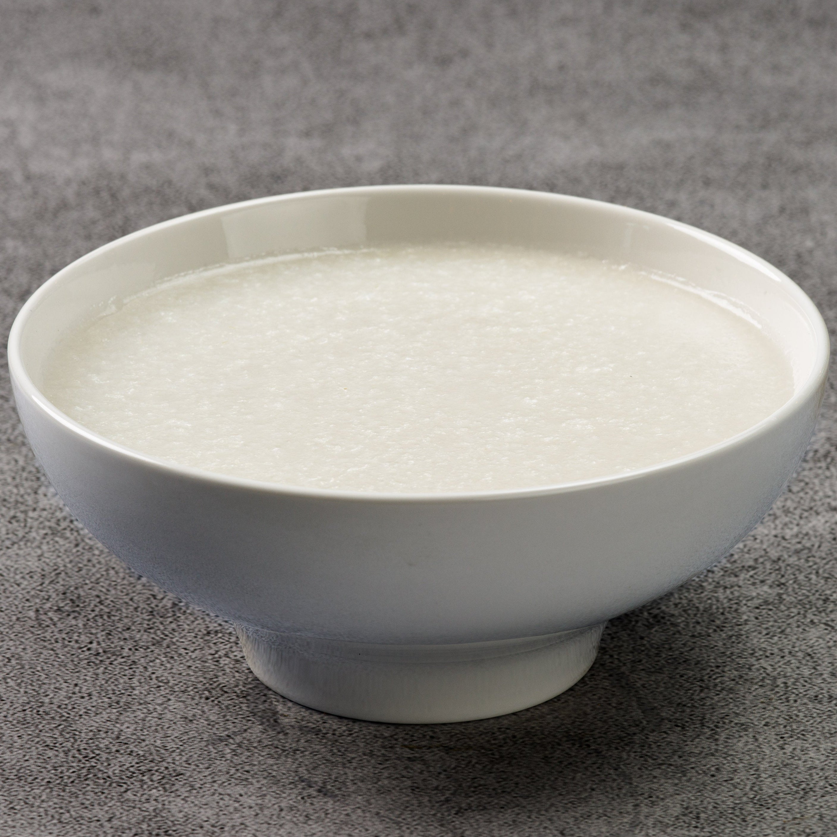 White congee in a bowl on a gray textured surface