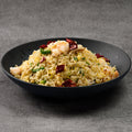 Black bowl of fried rice with shrimp and vegetables on a gray background