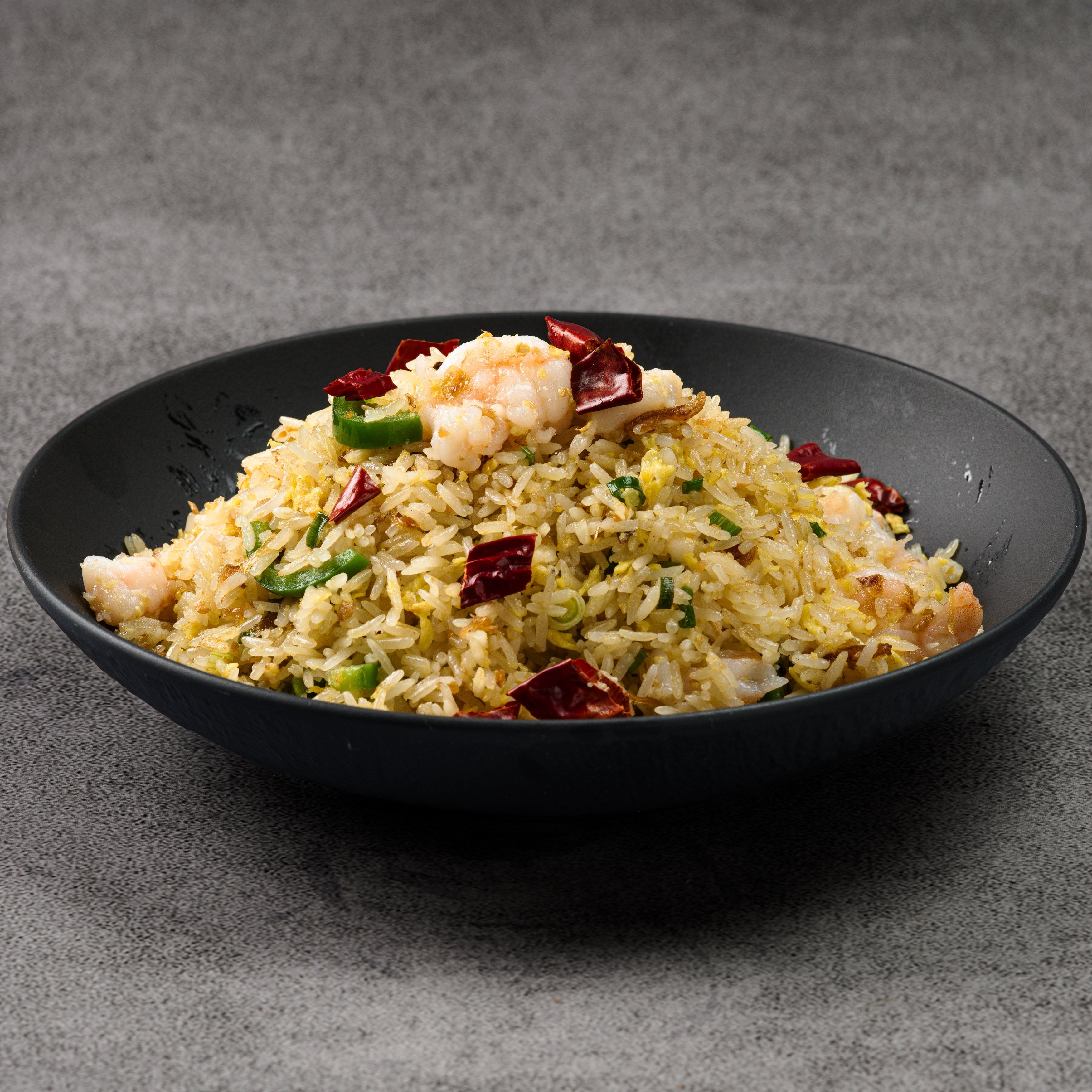 Black bowl of fried rice with shrimp and vegetables on a gray background